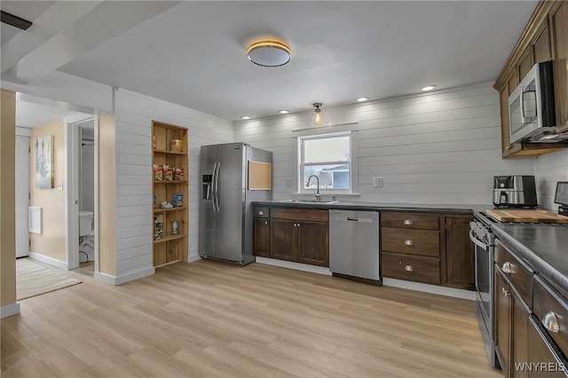 kitchen featuring stainless steel appliances, dark countertops, light wood-style floors, a sink, and dark brown cabinets