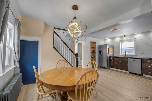 dining space featuring radiator, light wood finished floors, stairs, and a chandelier