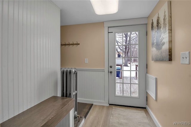 entryway featuring radiator, a healthy amount of sunlight, wood finished floors, and a wainscoted wall