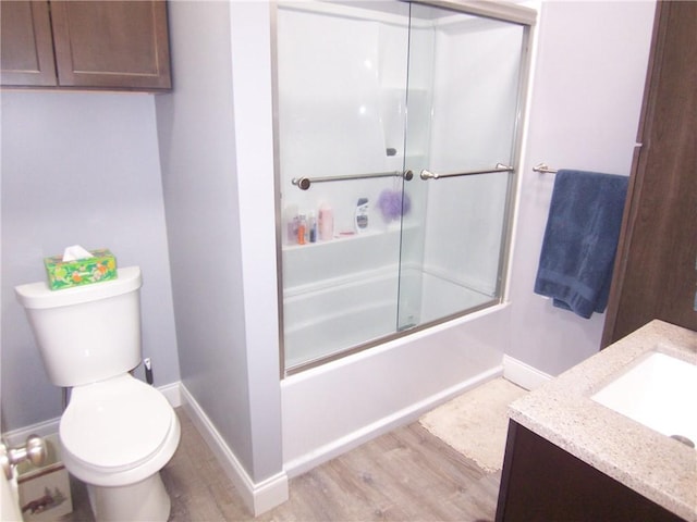 full bath featuring baseboards, toilet, enclosed tub / shower combo, wood finished floors, and vanity