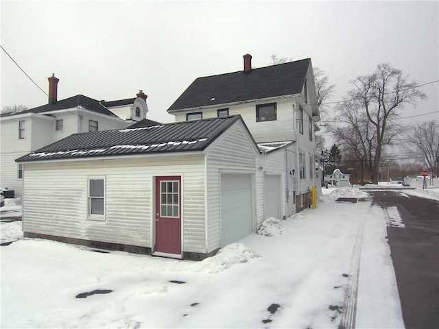 snow covered property featuring a garage, a standing seam roof, metal roof, and a chimney