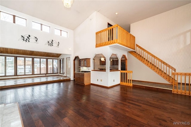 unfurnished living room with dark wood-type flooring, a towering ceiling, baseboards, and stairs