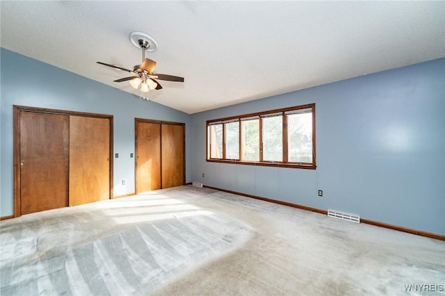 unfurnished bedroom featuring light carpet, baseboards, visible vents, lofted ceiling, and multiple closets