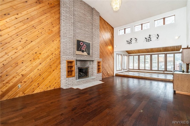 unfurnished living room featuring high vaulted ceiling, wood walls, a brick fireplace, and dark wood finished floors