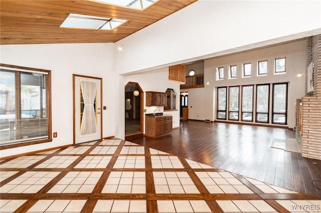 unfurnished living room with high vaulted ceiling, a skylight, baseboards, and wood finished floors