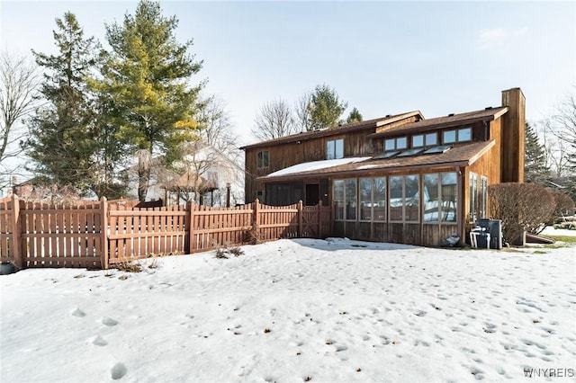 snow covered back of property featuring a sunroom and fence