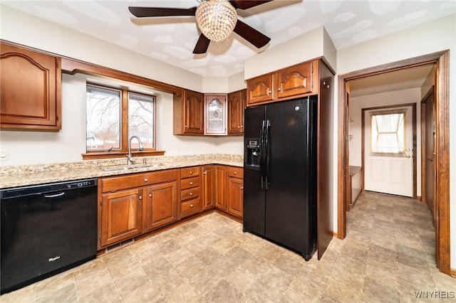 kitchen with brown cabinetry, a ceiling fan, a sink, light stone countertops, and black appliances