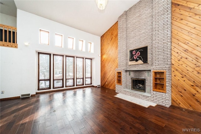 unfurnished living room featuring a brick fireplace, wood-type flooring, high vaulted ceiling, and wood walls