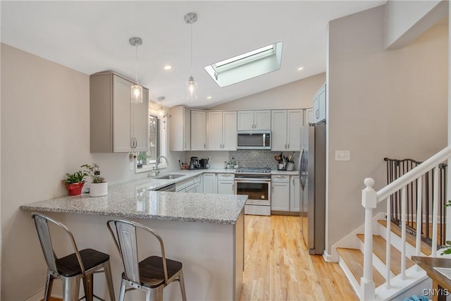 kitchen with vaulted ceiling with skylight, a peninsula, a sink, appliances with stainless steel finishes, and decorative backsplash