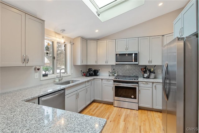 kitchen featuring lofted ceiling with skylight, light stone counters, appliances with stainless steel finishes, light wood-style floors, and a sink