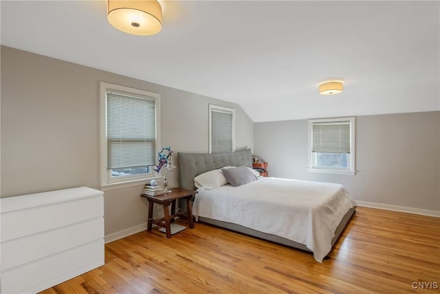 bedroom featuring multiple windows, baseboards, vaulted ceiling, and wood finished floors