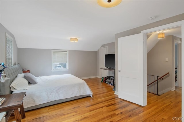 bedroom featuring light wood-type flooring, lofted ceiling, and baseboards