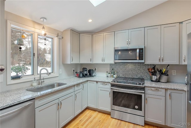 kitchen with stainless steel appliances, a sink, vaulted ceiling, decorative backsplash, and light wood finished floors