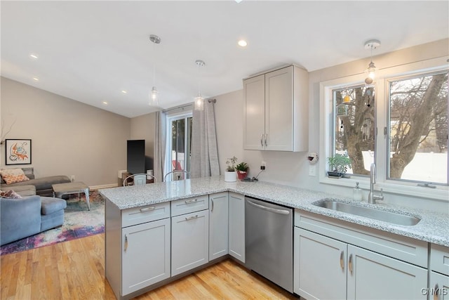 kitchen featuring dishwasher, a peninsula, a sink, and light wood-style floors