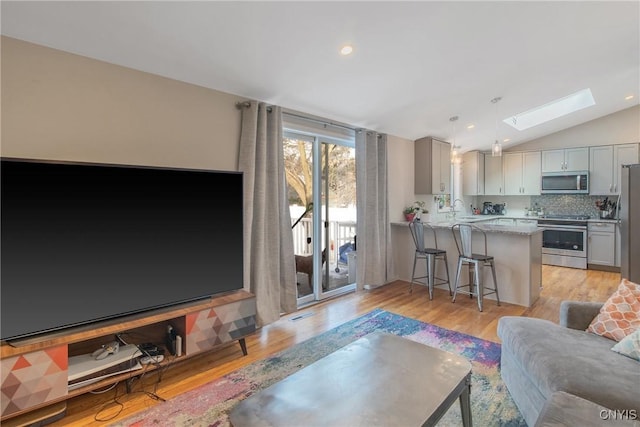 living area featuring lofted ceiling with skylight, recessed lighting, and light wood-style floors