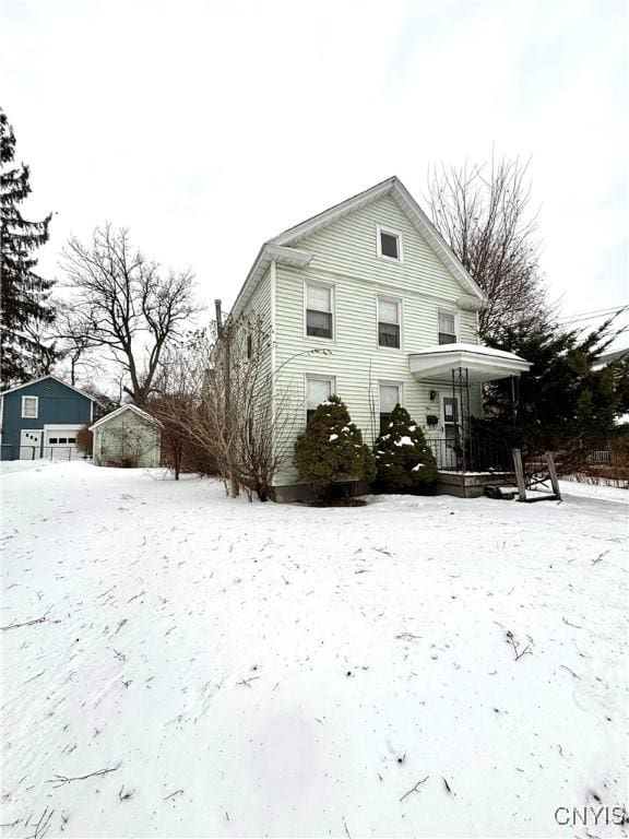 snow covered back of property featuring a porch and an outdoor structure