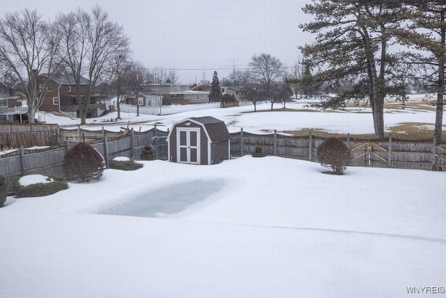 snowy yard with a shed, an outdoor structure, a fenced backyard, and a residential view