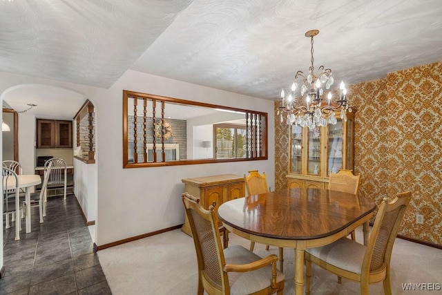 dining room with arched walkways, wallpapered walls, a chandelier, and baseboards