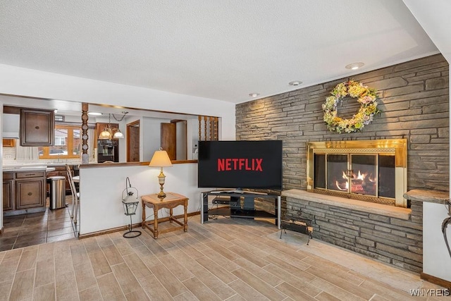 living room with wood tiled floor, a textured ceiling, and a stone fireplace