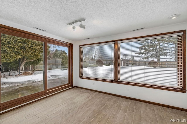 unfurnished sunroom featuring rail lighting, visible vents, and a wealth of natural light