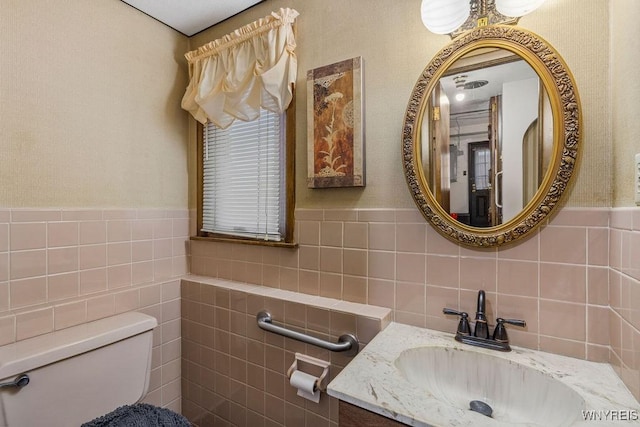 half bathroom with toilet, wainscoting, tile walls, and vanity