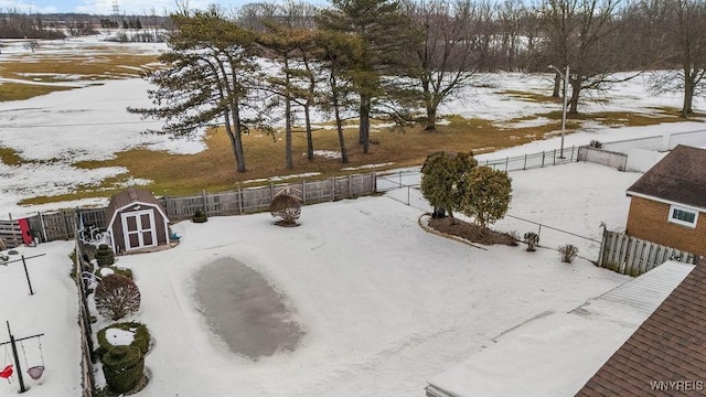 yard layered in snow featuring a storage shed, a fenced backyard, and an outbuilding