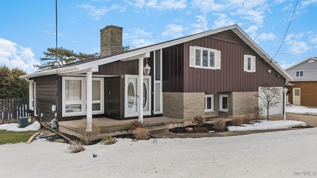 view of front of house featuring a garage, stone siding, a chimney, and central AC