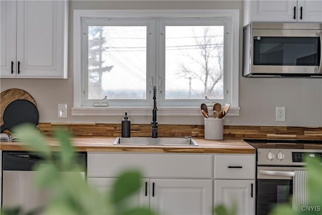 kitchen featuring white cabinets, butcher block counters, stainless steel appliances, and a sink