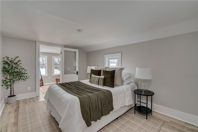 bedroom with lofted ceiling, light wood-style flooring, and baseboards