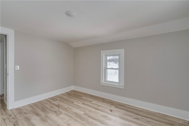 spare room featuring vaulted ceiling, light wood finished floors, and baseboards