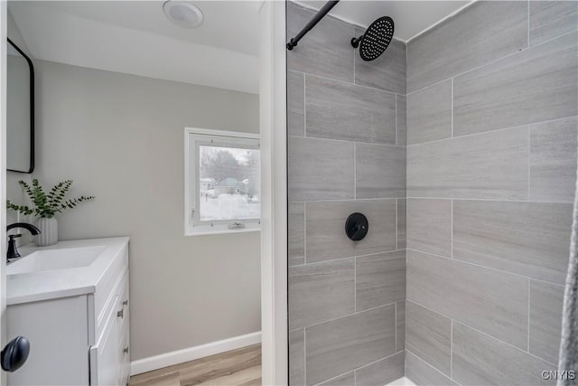 full bathroom featuring wood finished floors, a tile shower, vanity, and baseboards