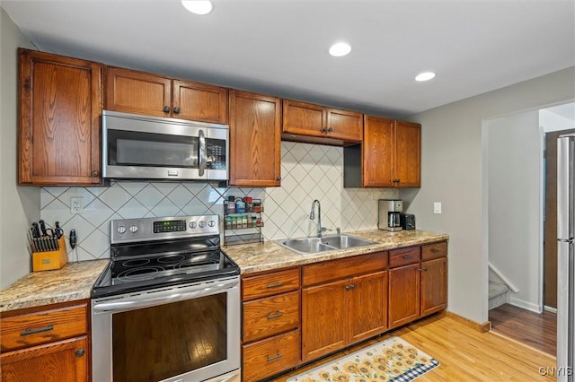 kitchen featuring appliances with stainless steel finishes, light wood-style floors, a sink, and backsplash