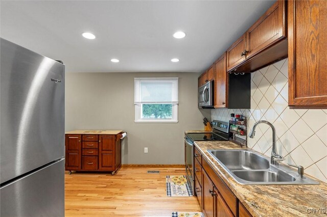 kitchen featuring brown cabinets, light wood finished floors, stainless steel appliances, and a sink