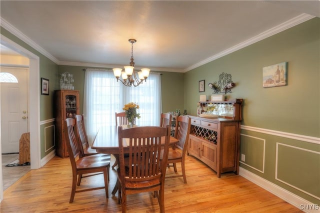 dining room featuring a notable chandelier, a decorative wall, a wainscoted wall, light wood-style floors, and ornamental molding