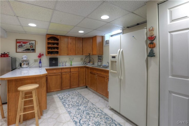 kitchen with brown cabinets, a peninsula, light countertops, white fridge with ice dispenser, and open shelves