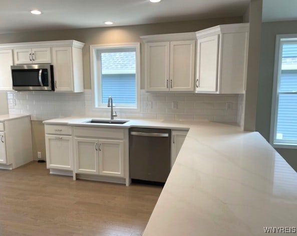 kitchen with white cabinets, appliances with stainless steel finishes, a sink, light wood-style flooring, and decorative backsplash