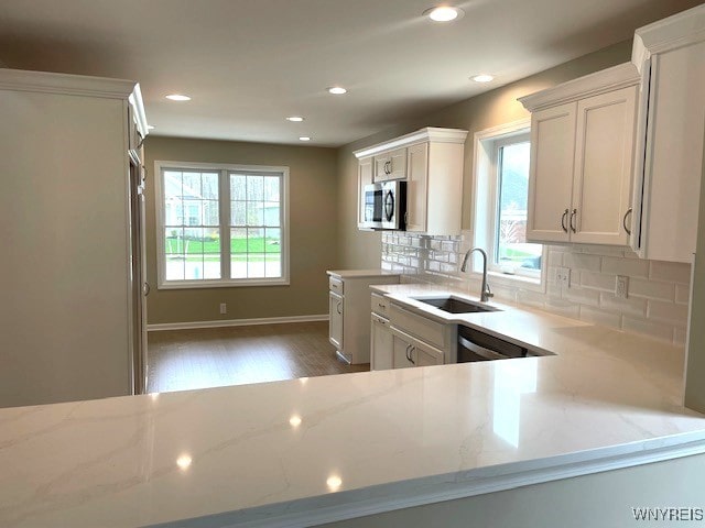 kitchen featuring light stone counters, a sink, decorative backsplash, and stainless steel microwave