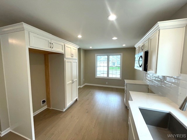 kitchen featuring wood finished floors, recessed lighting, stainless steel microwave, white cabinets, and a sink