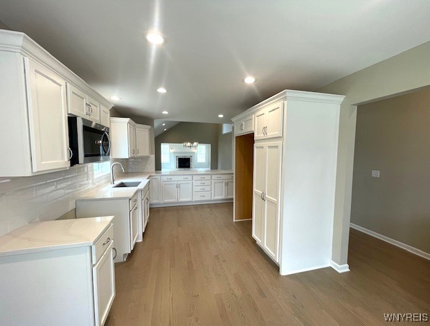 kitchen with white cabinets, a sink, stainless steel microwave, decorative backsplash, and wood finished floors