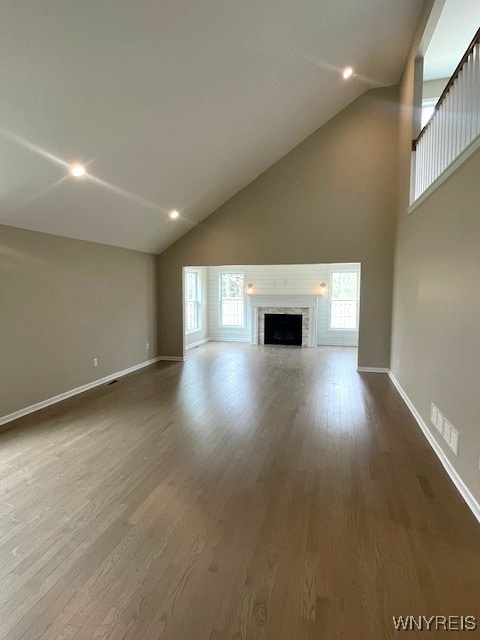 unfurnished living room featuring visible vents, wood finished floors, a healthy amount of sunlight, baseboards, and high vaulted ceiling