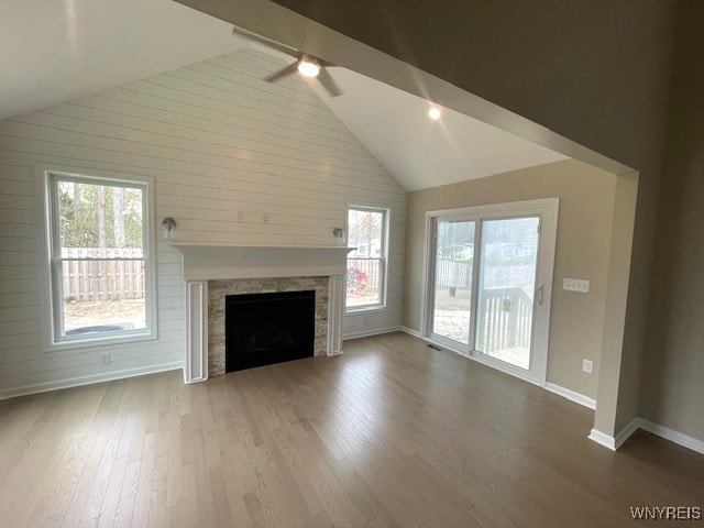 unfurnished living room with a stone fireplace, baseboards, wood finished floors, and high vaulted ceiling
