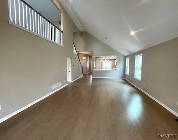 unfurnished living room featuring baseboards, visible vents, dark wood-style floors, and high vaulted ceiling