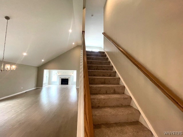 staircase with an inviting chandelier, a fireplace, high vaulted ceiling, baseboards, and wood finished floors