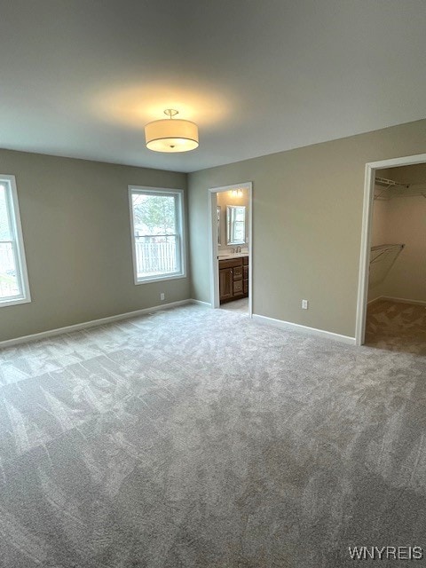 unfurnished bedroom featuring carpet floors, baseboards, a spacious closet, and ensuite bathroom