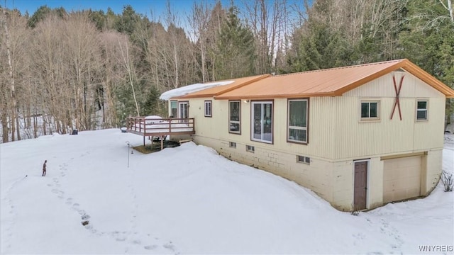 snow covered back of property with crawl space, an attached garage, a wooden deck, and metal roof