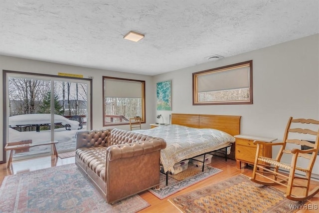 bedroom with access to outside, a textured ceiling, and wood finished floors