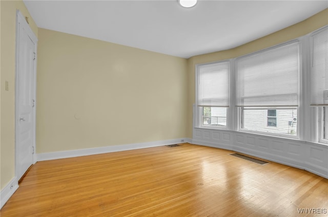 empty room with light wood-style flooring, visible vents, and baseboards