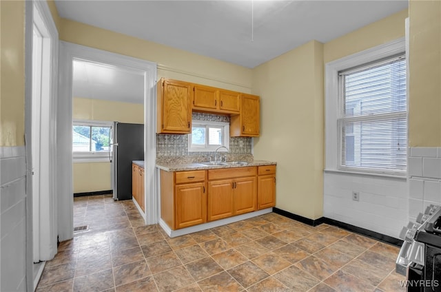 kitchen with light stone counters, tasteful backsplash, visible vents, freestanding refrigerator, and a sink