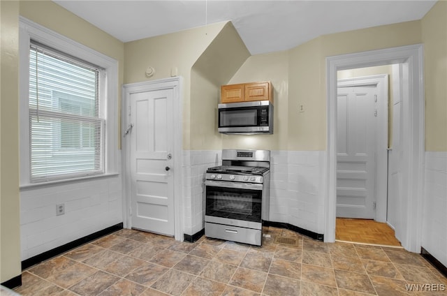 kitchen with stainless steel appliances, a wainscoted wall, and tile walls