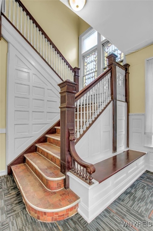 staircase featuring carpet, a wainscoted wall, and a decorative wall